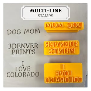 May include: Three yellow rectangular stamps with raised text reading DOG MOM, 3DENVER PRINTS, and I LOVE COLORADO. The corresponding impressions are visible to the left of each stamp, showing the text in a standard orientation on a light surface.