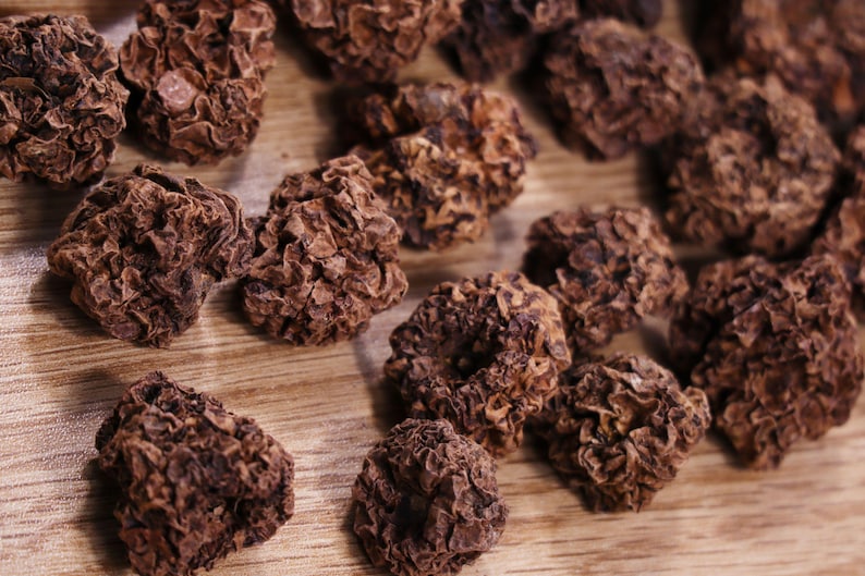 May include: Close-up of dried, brown, wrinkled fruit pieces on a wooden surface. The fruit pieces are irregularly shaped and have a rough texture.