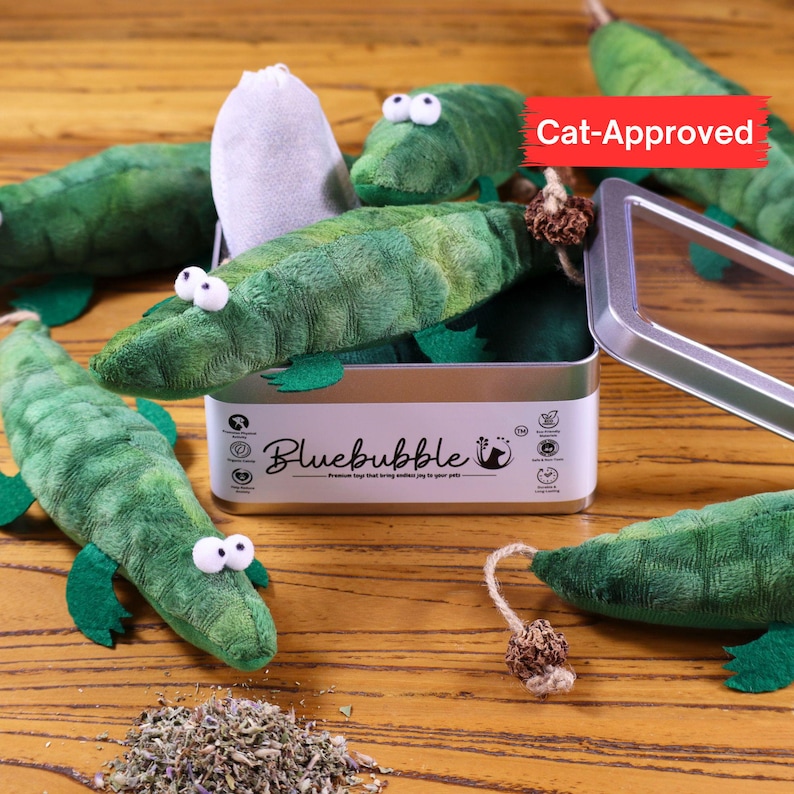 Peut inclure: Un ensemble de cinq jouets pour chat en forme d'alligator en peluche verte dans une bo&icirc;te en &eacute;tain argent&eacute;e avec le texte "Bluebubble" et "Premium toys that bring endless joy to your pet". La bo&icirc;te est ouverte et les jouets sont &eacute;parpill&eacute;s autour d'elle. Les jouets ont une poche de catnip &agrave; l'int&eacute;rieur et une queue en ficelle. Le texte "Cat-Approved" est dans un encadr&eacute; rouge sur le c&ocirc;t&eacute; droit de l'image.