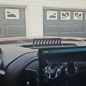 Può includere: Una copertura nera rettangolare per la ventilazione del cruscotto dell'auto con un design a fessure. Il cruscotto presenta anche un ampio touchscreen che mostra l'ora come 19:31. L'interno è nero con inserti in pelle.