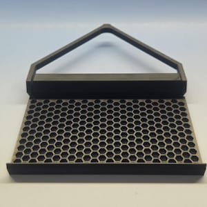 May include: A black and gray honeycomb-patterned tray with a handle. The tray has a rectangular base with a series of hexagonal holes. The handle is a triangular shape. The product is likely a kitchen or home decor item.