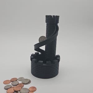 May include: A black, 3D-printed coin tower shaped like a castle with a spiral ramp. A coin is on the ramp, and a pile of coins sits at the base. The tower is made of brick-like segments.