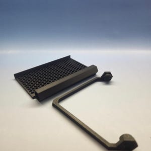 May include: A dark gray, 3D-printed component with a honeycomb-patterned grill and an L-shaped support arm. The arm has hexagonal end pieces. The items are set against a white surface with a blue gradient background.