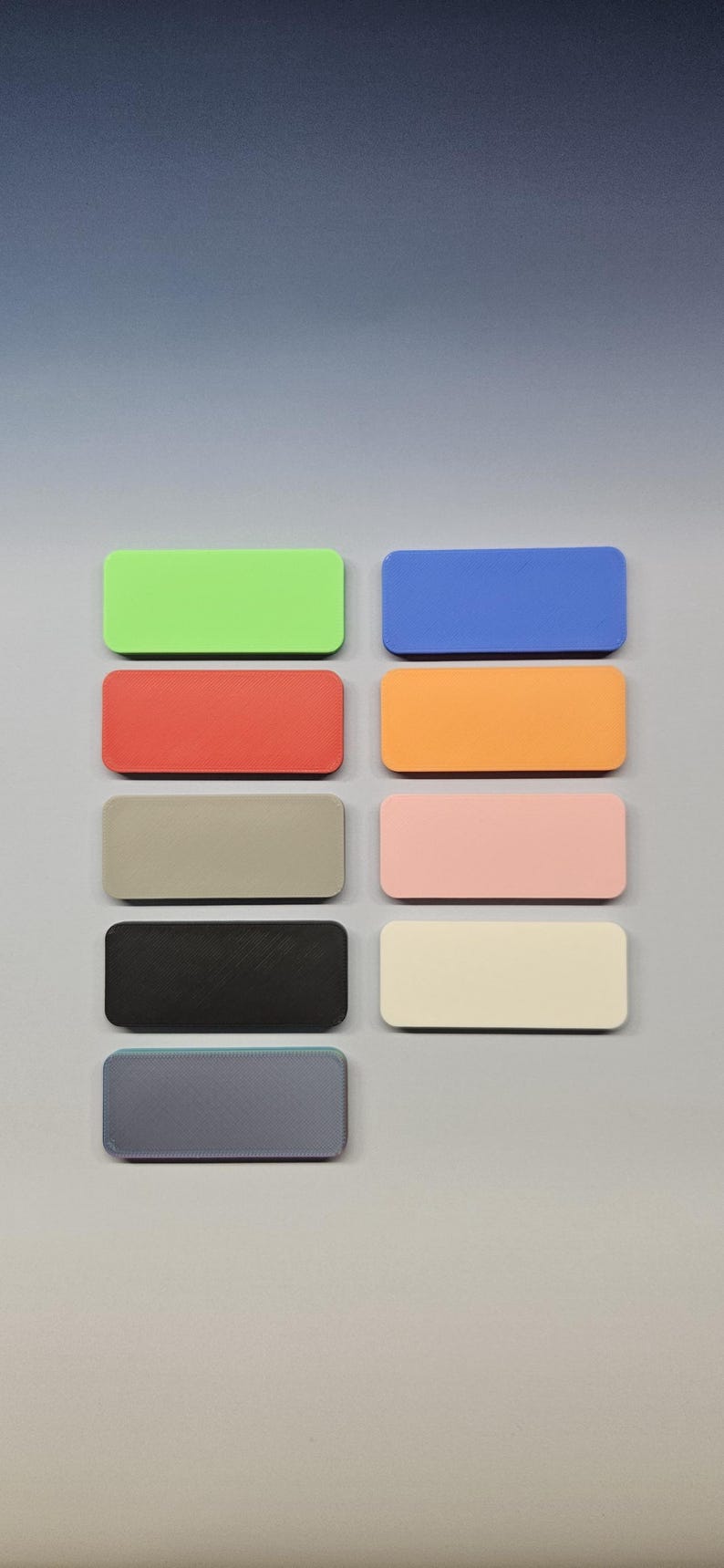 May include: A collection of ten rectangular objects in various colors, including green, blue, red, orange, gray, pink, black, and cream. The objects are arranged in two rows of five on a light gray surface.