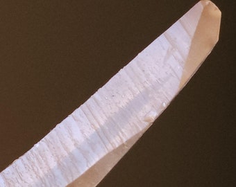 May include: A clear quartz crystal with a pointed tip and striations running along its length.