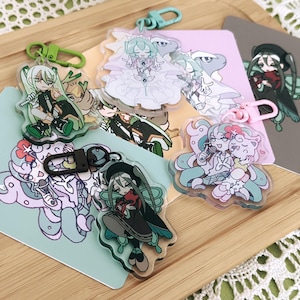 May include: A set of 8 colorful acrylic charms featuring anime-style characters. The charms are attached to keychains and feature various designs, including a girl with green hair, a girl with pink hair, and a girl with blue hair. The charms are perfect for adding a touch of personality to your bag or keys.