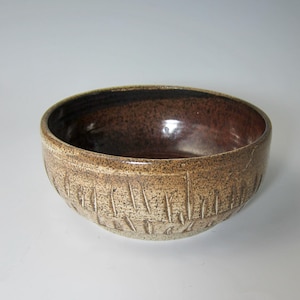 May include: A brown ceramic bowl with a textured, white rim and a brown interior. The bowl has a unique design of vertical lines on the outside.