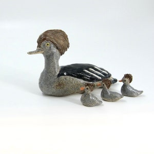 May include: A ceramic figurine of a grey and black duck with a brown crest, surrounded by three smaller grey ducklings.