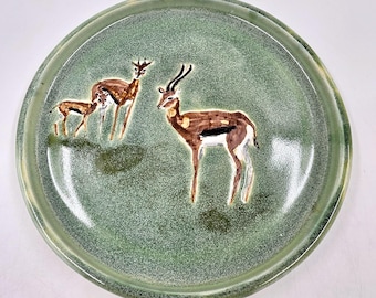 Plato de porcelana torneada en torno con diseño de gacelas de Thomson sobre fondo verde satinado.