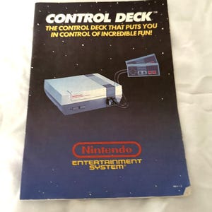 May include: A vintage Nintendo Entertainment System advertisement. The cover features the text "CONTROL DECK" and "THE CONTROL DECK THAT PUTS YOU IN CONTROL OF INCREDIBLE FUN!" with an illustration of the console and controller. The Nintendo logo is also visible.