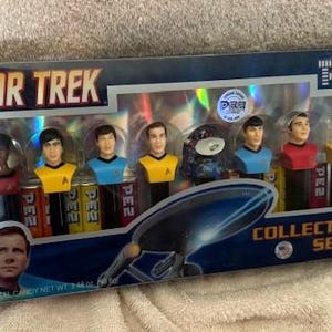 May include: A Star Trek Collector's Series PEZ dispenser set. The set includes seven character dispensers in a clear plastic package. The package has the Star Trek logo and the words "Collector's Series". The total candy net weight is 3.48 oz.
