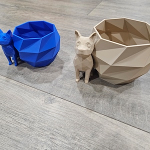 May include: Two geometric planters, one blue and one beige, with a small, beige, geometric dog figurine in front of the beige planter.