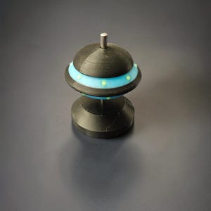 May include: A black and blue decorative spinning top with a silver post. The top has a rounded shape with a light blue band and small green dots. The base is also black and has a geometric design.