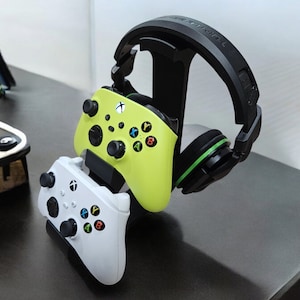 May include: A black headset with green accents is displayed on a stand with two Xbox controllers, one white and one green.