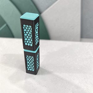 May include: A tall, rectangular, black vertical object with a light blue top and a repeating honeycomb pattern cut out on all four sides, revealing a light blue interior layer. The structure consists of two stacked segments.