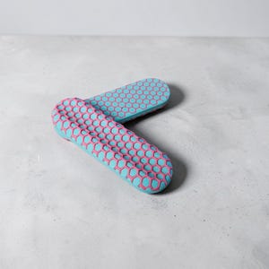 May include: Two elongated, rounded objects featuring a bright light blue base color with a raised, textured pink honeycomb pattern covering the top surface. The objects are positioned at an angle, with one partially overlapping the other.