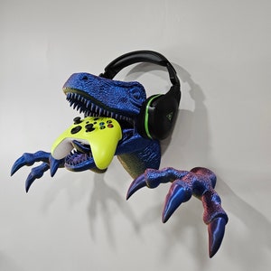 May include: A blue and purple dinosaur head wall mount with a green and black headset hanging from its mouth and a yellow video game controller in its jaws.