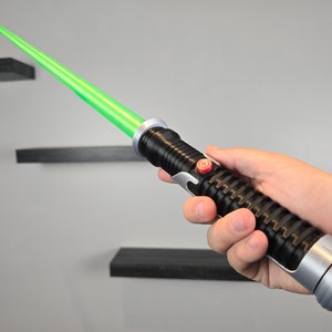 May include: A black and silver lightsaber toy with a green blade. The lightsaber has a red button on the side.
