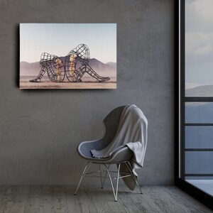 May include: A black and white photo of a metal sculpture of three figures in a desert landscape. The figures are intertwined and appear to be embracing.