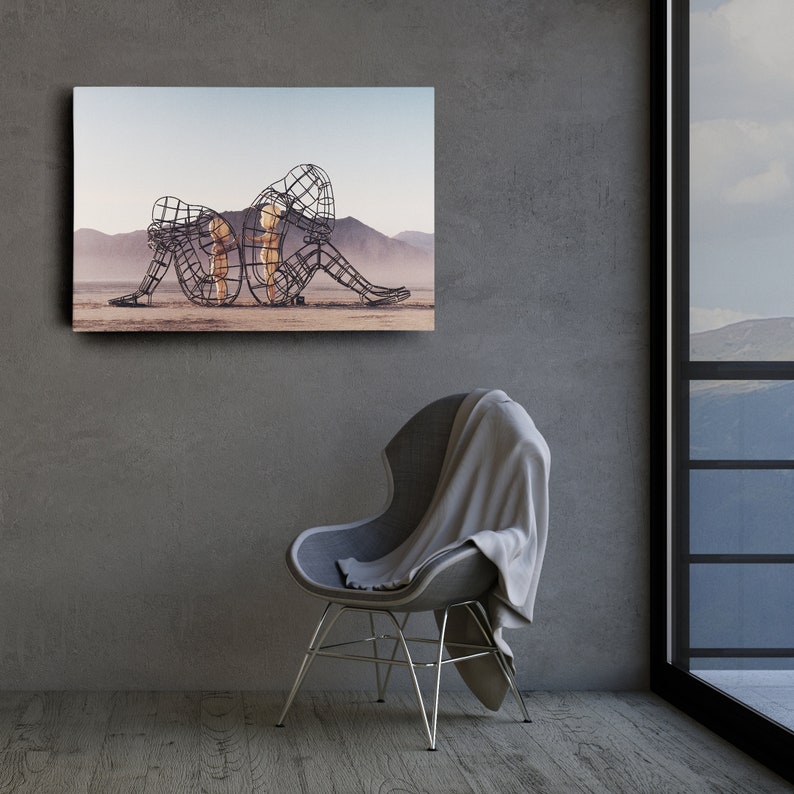 May include: A black and white photo of a metal sculpture of three figures in a desert landscape. The figures are intertwined and appear to be embracing.