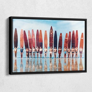 May include: A vintage photograph of a group of men standing on a beach with surfboards. The men are wearing swimsuits and are holding their surfboards. The surfboards are all different colors and have different designs. The beach is sandy and the water is blue.