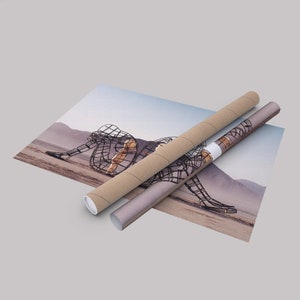 May include: A rolled up poster featuring a black metal sculpture of two figures in a desert landscape. The poster is being unrolled from a brown cardboard tube.