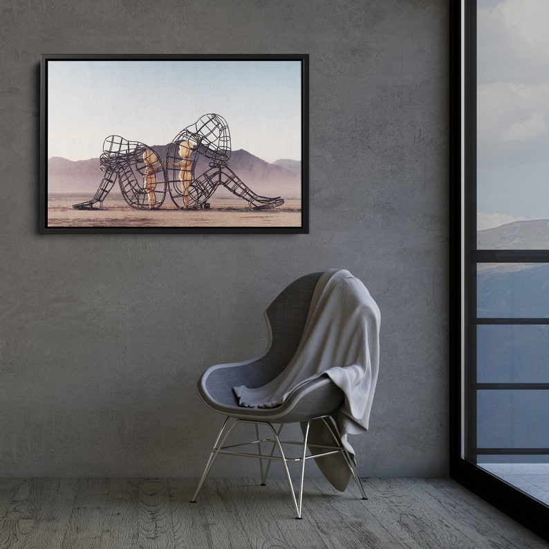 May include: A framed photograph of a metal sculpture of two figures, one larger than the other, sitting on a desert landscape. The sculpture is made of wire and appears to be a representation of a mother and child.