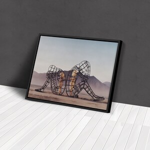 May include: Two figures made of wire mesh stand in a desert landscape. The figures are posed as if they are embracing, with one figure's arms wrapped around the other's waist. The figures are made of a dark metal and have a rusted appearance.