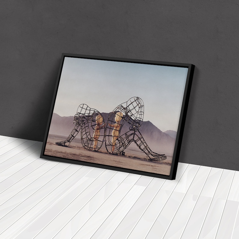 May include: Two figures made of wire mesh stand in a desert landscape. The figures are posed as if they are embracing, with one figure's arms wrapped around the other's waist. The figures are made of a dark metal and have a rusted appearance.