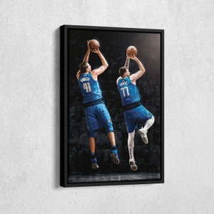May include: A framed canvas print featuring two basketball players in blue uniforms, mid-jump, shooting a basketball. One player wears number 41, the other number 77. The background is a blurred crowd, with a black frame.