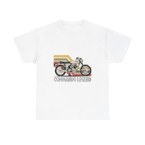 Puede incluir: Camiseta blanca con una ilustración de motocicleta vintage y el texto "COMMANDO LEGEND". La motocicleta está representada en un estilo retro con colores beige, rojo, amarillo y verde. El diseño incluye rayas horizontales.