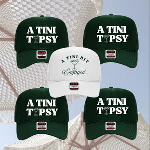 Puede incluir: Cinco gorras de béisbol. Cuatro son de color verde oscuro con "A TINI TYPSY" en blanco. Una es blanca con "A TINI BIT Engaged". Todas tienen una parte trasera de malla y una pequeña etiqueta.