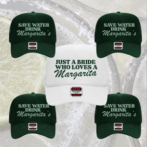Puede incluir: Se muestran varias gorras de béisbol. Cuatro son de color verde oscuro con el texto "Save Water Drink Margarita's" en blanco. Una gorra blanca tiene el texto "Just a Bride Who Loves a Margarita" en verde.