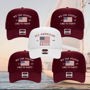 Puede incluir: Cinco gorras de camionero con diseños patrióticos. Cuatro son de color burdeos con "WE THE PEOPLE LIKE TO PARTY" y una bandera americana. Una gorra blanca dice "ALL AMERICAN BRIDE" con una bandera. Todas las gorras tienen etiquetas "OTTO".