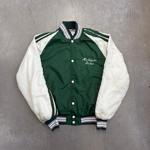 May include: A forest green and white satin varsity jacket featuring white raglan sleeves, a snap-button front closure, and striped ribbed cuffs and collar. The text Michigan State is embroidered in white script on the upper left chest.