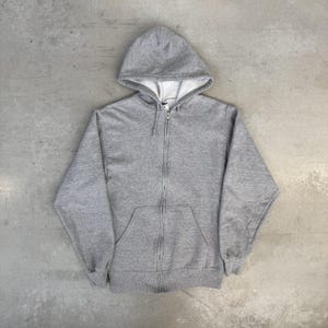 May include: A gray zip-up hoodie with a hood and a front pocket. The hoodie is made of a soft material and has a full-length zipper. The interior of the hood is white.