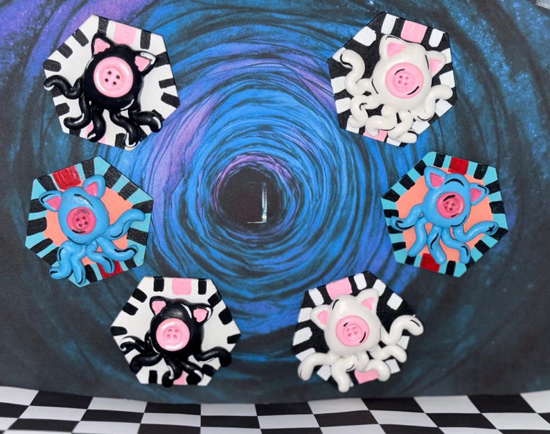 May include: A collection of whimsical, handmade octopus-pig hybrid art pieces. Each piece features a pink button nose, a button eye, and tentacles. The octopuses are in black, white, and blue, set against a hexagonal background with a striped border.