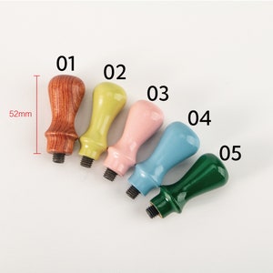 May include: Five wooden stamp handles in different colors: brown, yellow, pink, blue, and green. The handles are approximately 5.2 cm long.