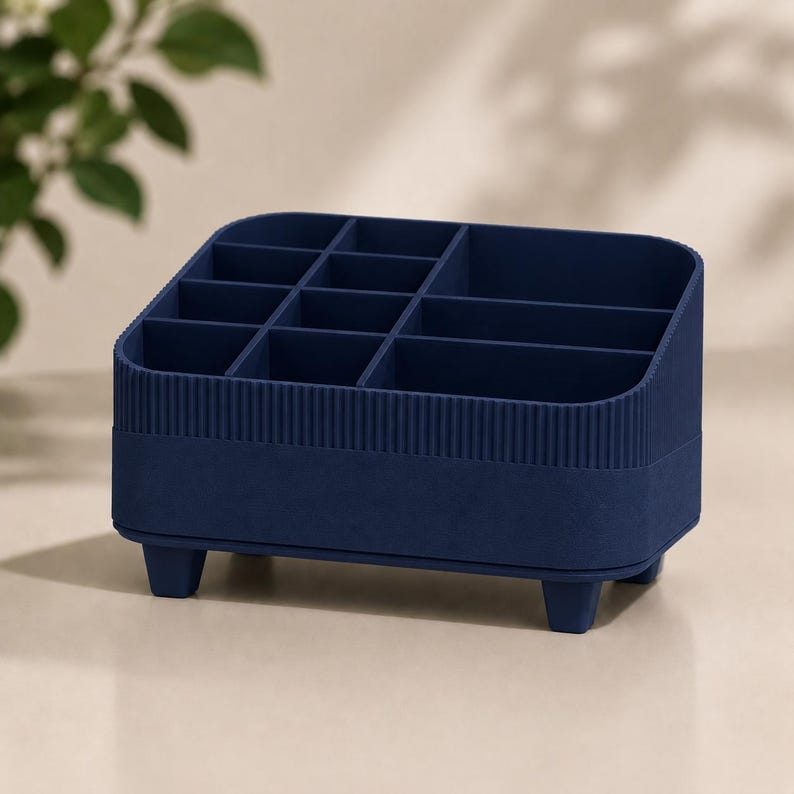 May include: A dark blue desk organizer featuring multiple compartments of varying sizes for storage. The exterior has a ribbed texture on the upper section and a smooth finish on the lower base, supported by four small, sturdy feet at the corners.