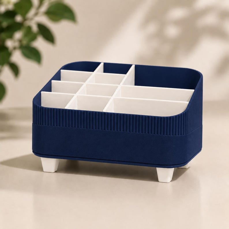May include: A navy blue desk organizer with a ribbed exterior texture and white interior dividers. The rectangular container features multiple compartments of varying sizes for storage and is supported by four small white feet at the base.