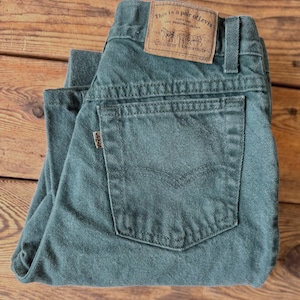 Op de afbeelding: Een paar teal Levi's jeans, opgevouwen op een houten oppervlak. De jeans hebben een klassiek ontwerp met vijf zakken, een klein Levi's-label en een bruin leren label met de tekst "This is a pair of Levi's THE ORIGINAL JEANS".