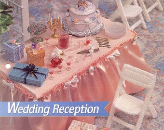 May include: A miniature wedding reception scene with a three-tiered cake, gifts, and white chairs. The table is draped in pink fabric and adorned with small glasses and a candelabra. The text "Wedding Reception" is displayed.