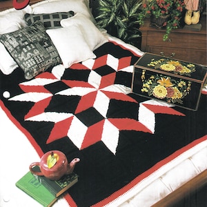 May include: A handmade afghan with a geometric star pattern in red, white, and black. The afghan is on a bed with pillows and a decorative chest. The text "BROKEN STAR AFGHAN" is visible.