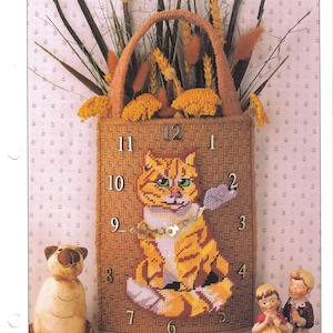May include: A brown canvas tote bag with a cat and mouse clock design. The cat is orange and white with green eyes. The mouse is gray and is holding a piece of cheese. The clock face has numbers 1 through 12. The tote bag has a brown handle and is decorated with dried flowers.