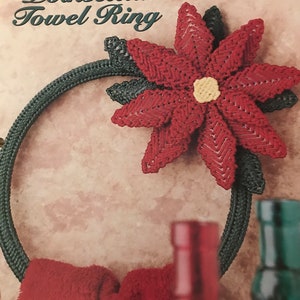 May include: A Poinsettia Towel Ring, a craft project, features a red poinsettia flower with a yellow center and dark green leaves. The ring is dark green and holds a red towel. The text "Poinsettia Towel Ring" is visible.