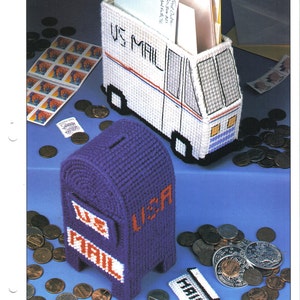 May include: A plastic canvas mail desk set featuring a white delivery truck mail holder with US MAIL text and a purple mailbox bank with US MAIL text. The set includes a small white mail piece and a sheet of postage stamps, all crafted from yarn.