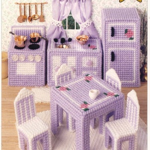 May include: A dollhouse kitchen set in shades of lavender and white, featuring a stove, refrigerator, sink, table, and chairs. The set includes miniature copper pots and pans, and the text "Dollhouse Kitchen" is visible.