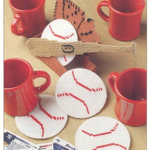May include: A set of five white plastic canvas coasters with red stitching, shaped like baseballs. The coasters are arranged around two red mugs with white handles. A brown plastic canvas bat is lying on top of the coasters. The coasters are surrounded by baseball trading cards.