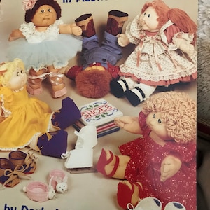 May include: A book cover titled "DOLL SHOES in plastic canvas" featuring several dolls and various doll shoes. The dolls are dressed in different outfits, and the shoes are in various styles and colors. The author's name, Darla J. Fanton, is also visible.