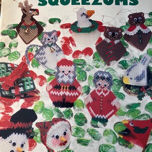 May include: A plastic canvas Christmas ornament kit featuring a variety of designs, including a snowman, Santa Claus, a goose, a cat, and a cardinal. The kit is titled "Christmas Squeezums" and is by Carol Wilson Mansfield.